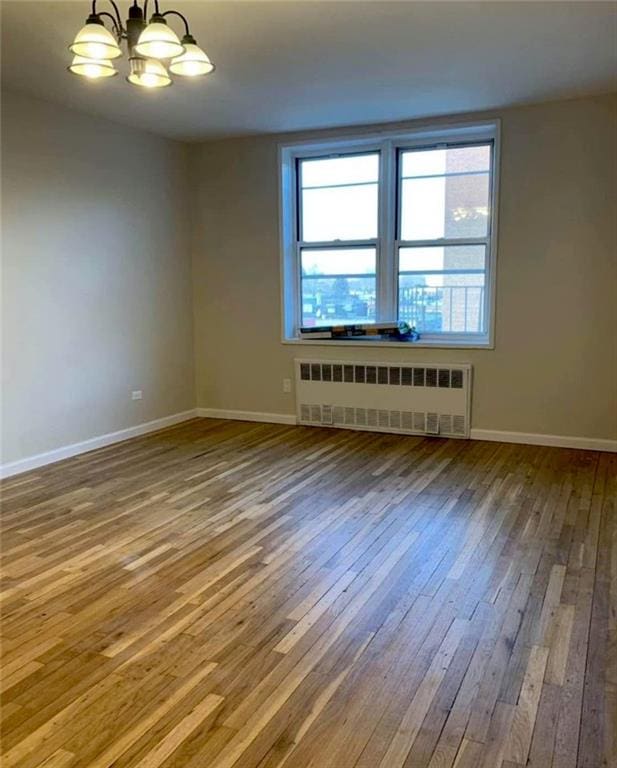 empty room featuring radiator heating unit, hardwood / wood-style flooring, a chandelier, and baseboards