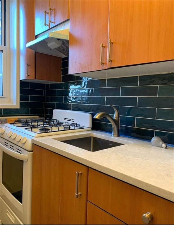 kitchen with under cabinet range hood, white range with gas cooktop, tasteful backsplash, and light countertops