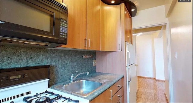 kitchen featuring a sink, tasteful backsplash, freestanding refrigerator, black microwave, and gas range