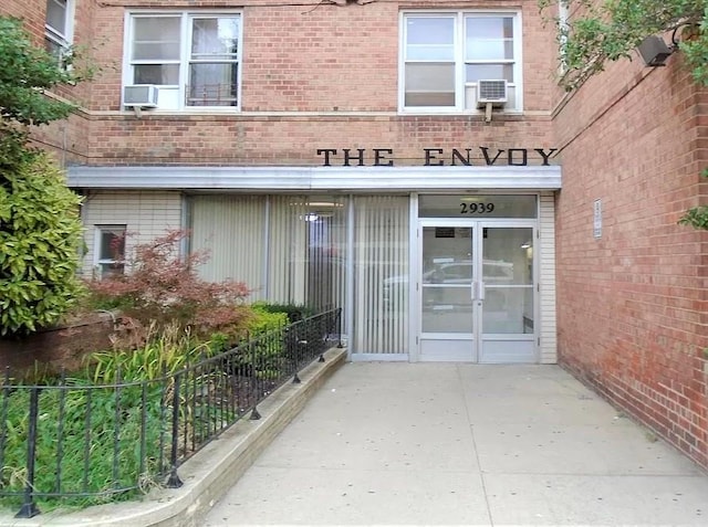 view of exterior entry featuring brick siding and fence