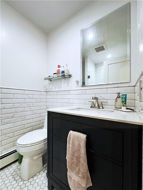 bathroom with visible vents, toilet, vanity, a baseboard heating unit, and tile walls