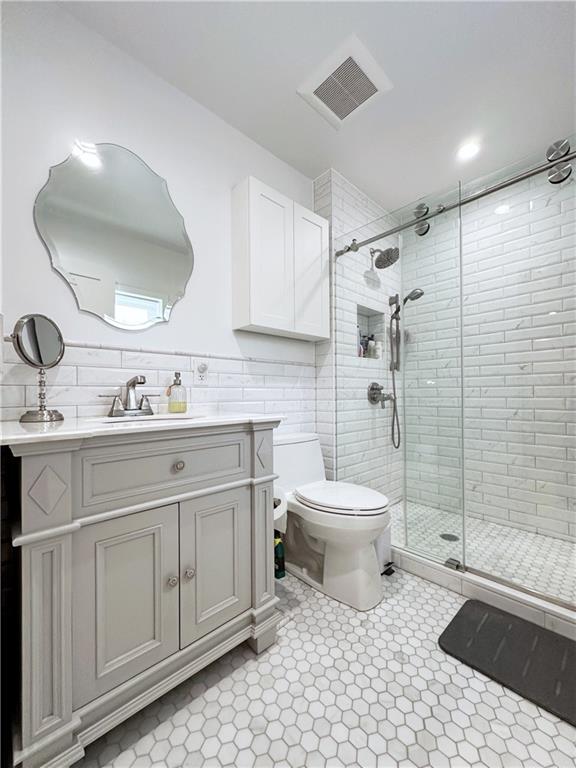 bathroom featuring tile walls, visible vents, toilet, a stall shower, and vanity