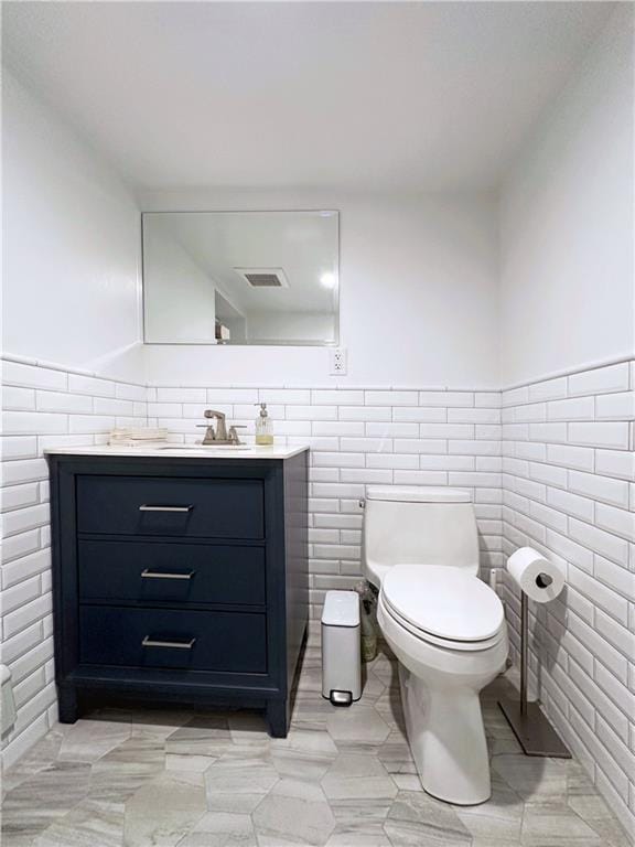 bathroom with a wainscoted wall, tile walls, visible vents, toilet, and vanity