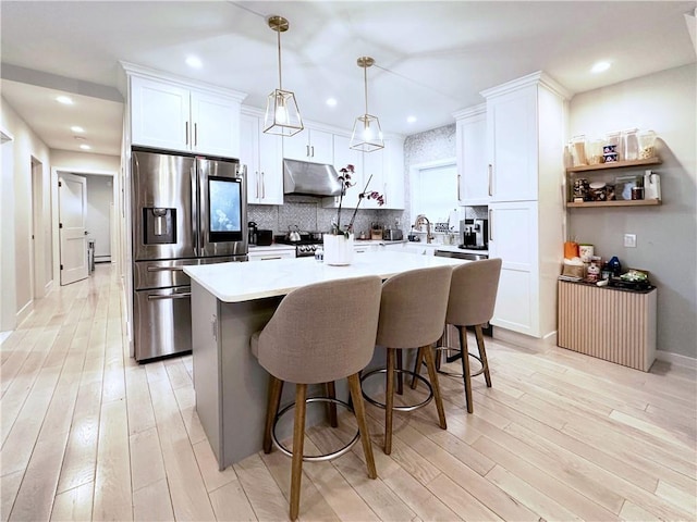 kitchen featuring under cabinet range hood, a center island, light wood-style flooring, and stainless steel fridge with ice dispenser