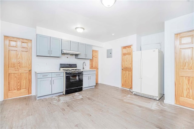 kitchen with light wood-type flooring, freestanding refrigerator, under cabinet range hood, and gas stove