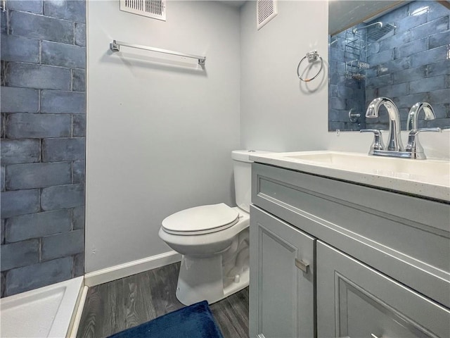 bathroom featuring toilet, tiled shower, wood finished floors, and visible vents