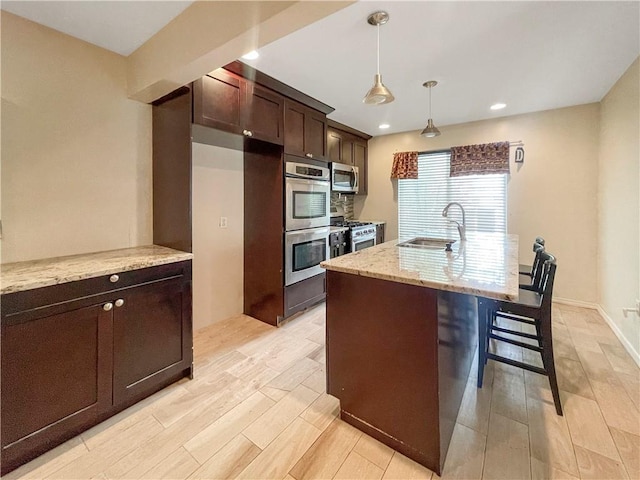 kitchen featuring appliances with stainless steel finishes, a sink, light wood finished floors, and light stone countertops