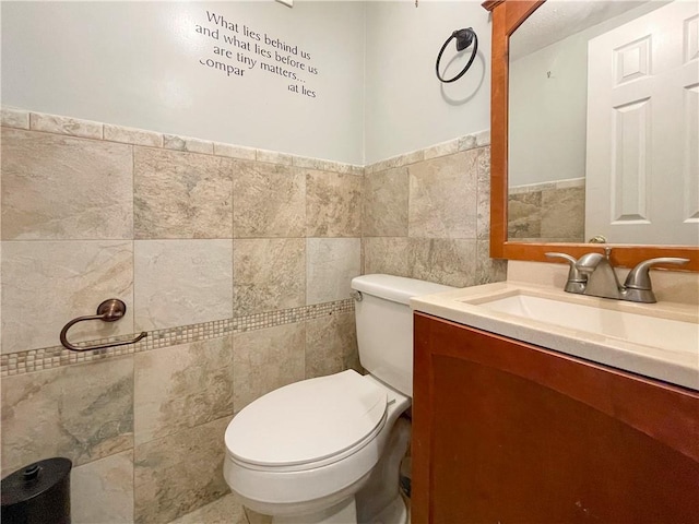 bathroom featuring toilet, vanity, and tile walls