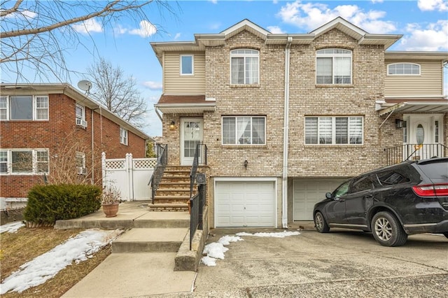 view of property featuring driveway, an attached garage, fence, and brick siding