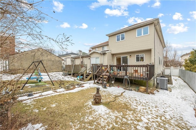 snow covered rear of property with a fenced backyard, cooling unit, and a wooden deck