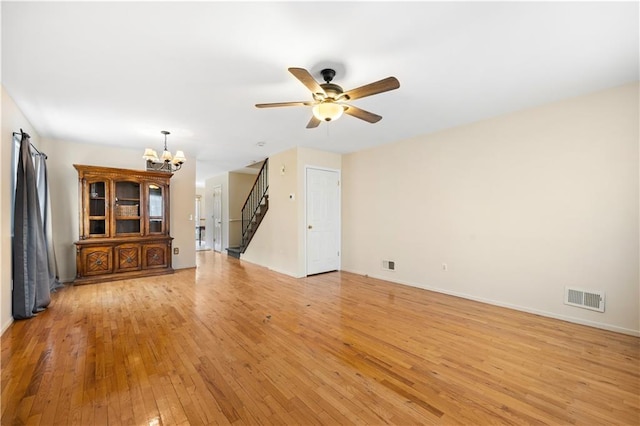 unfurnished living room with light wood finished floors, baseboards, visible vents, stairs, and ceiling fan with notable chandelier