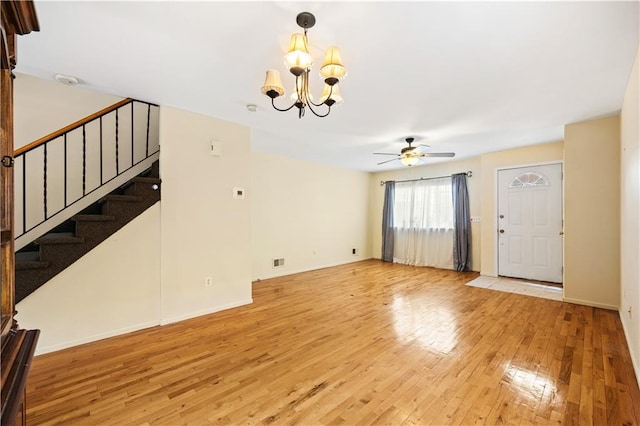 unfurnished living room featuring light wood-type flooring, stairs, baseboards, and ceiling fan with notable chandelier