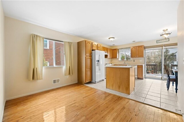 kitchen featuring light wood finished floors, white refrigerator with ice dispenser, visible vents, a center island, and light countertops