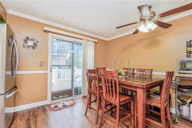 dining room with baseboards, ceiling fan, wood finished floors, and crown molding