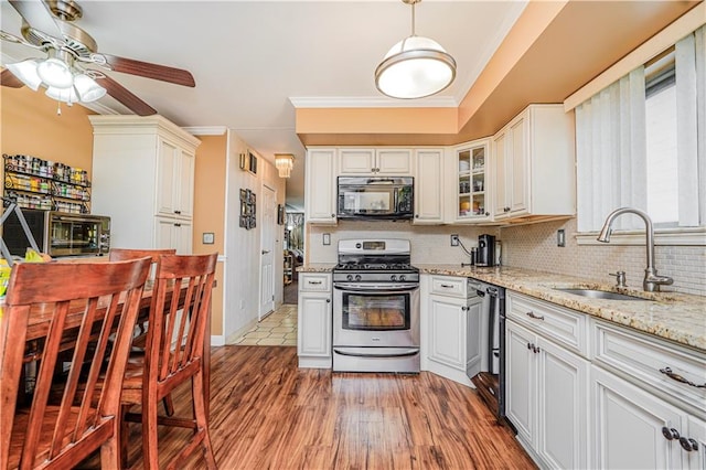 kitchen featuring black microwave, a sink, ornamental molding, backsplash, and stainless steel range with gas stovetop