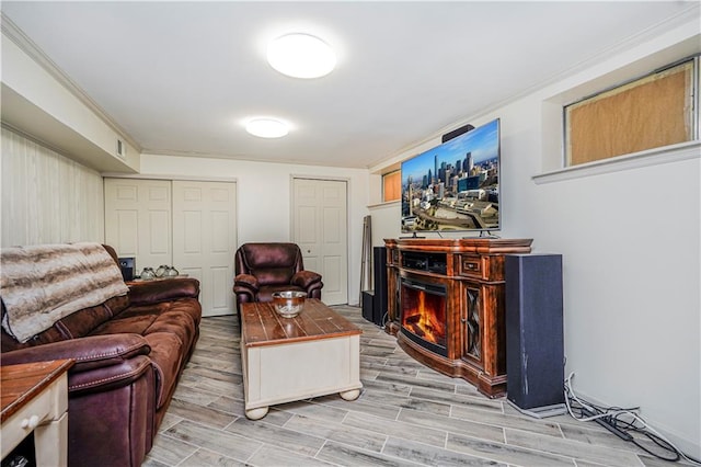 living room featuring a warm lit fireplace, crown molding, and wood finish floors