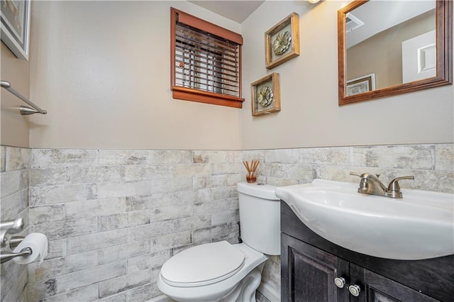 half bath with toilet, a wainscoted wall, tile walls, and vanity