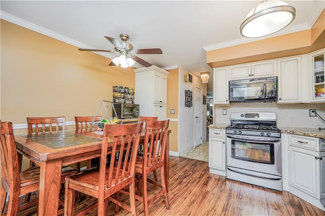 kitchen featuring stainless steel range with gas cooktop, crown molding, tasteful backsplash, light wood-style flooring, and black microwave