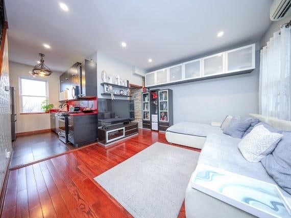 living room featuring a wall unit AC, baseboards, wood finished floors, and recessed lighting