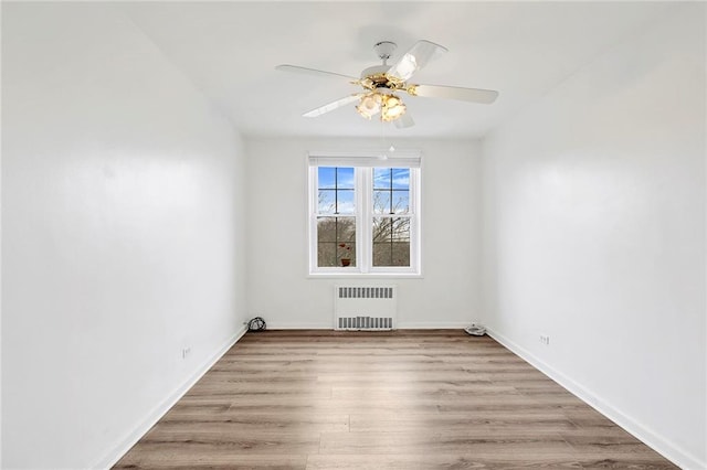 empty room with radiator heating unit, wood finished floors, a ceiling fan, and baseboards