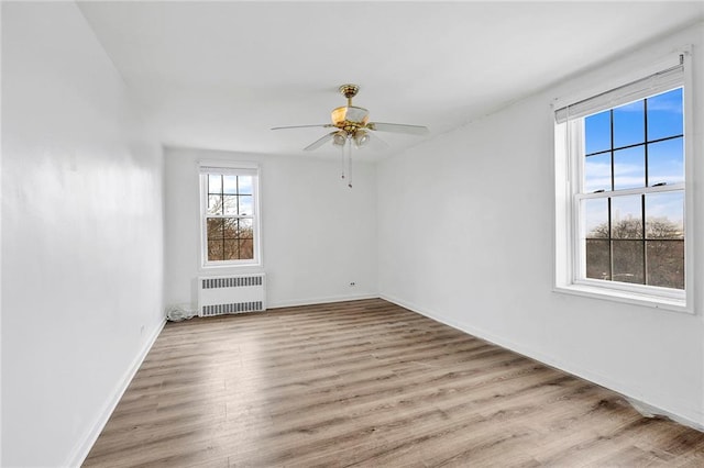 unfurnished room with radiator, ceiling fan, baseboards, and wood finished floors