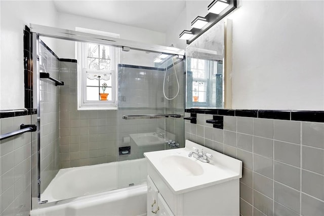 bathroom with a wainscoted wall, combined bath / shower with glass door, tile walls, and vanity