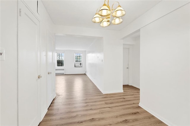 corridor with light wood-style floors, baseboards, and an inviting chandelier