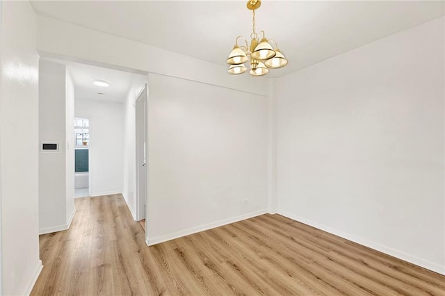 spare room with light wood-type flooring, a notable chandelier, and baseboards