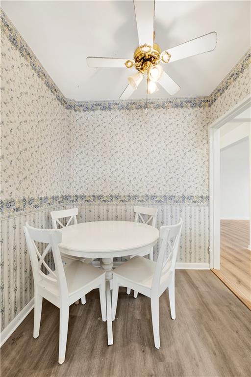 unfurnished dining area featuring wallpapered walls, a ceiling fan, baseboards, and wood finished floors