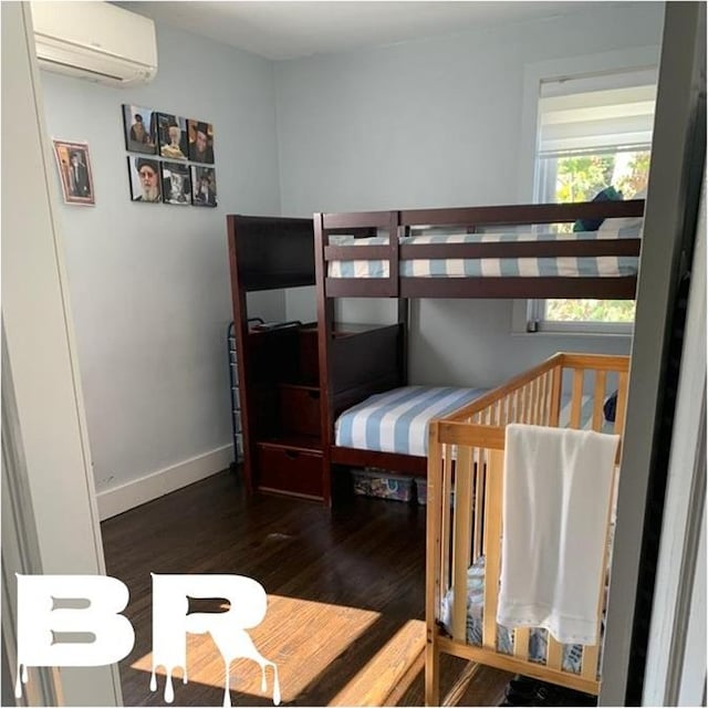 bedroom with wood finished floors, baseboards, and a wall unit AC