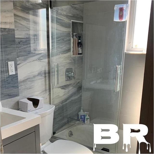 bathroom with combined bath / shower with glass door, toilet, tile walls, and vanity