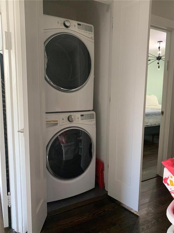 laundry room featuring laundry area, stacked washer and dryer, and dark wood-style floors