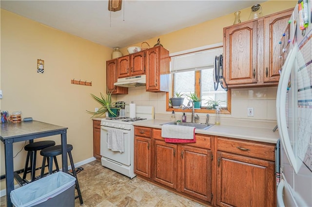 kitchen with light countertops, decorative backsplash, a sink, white appliances, and under cabinet range hood