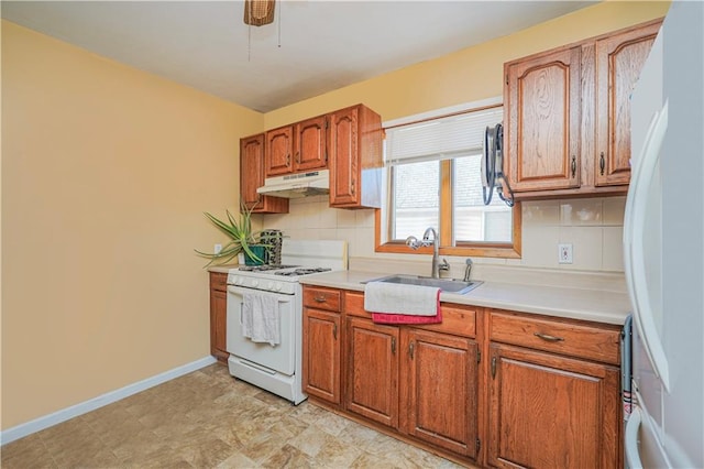 kitchen with white appliances, tasteful backsplash, brown cabinets, under cabinet range hood, and a sink