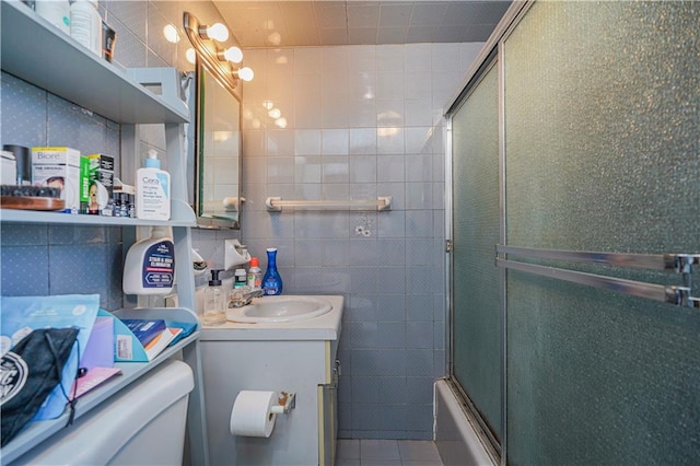 bathroom with toilet, shower / bath combination with glass door, tile patterned floors, vanity, and tile walls