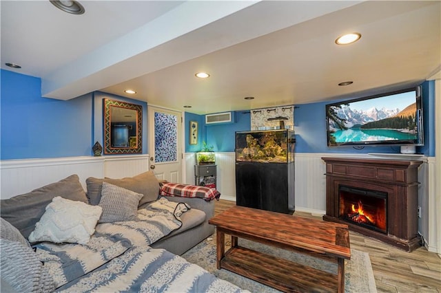 living room with a wainscoted wall, a lit fireplace, wood finished floors, and recessed lighting