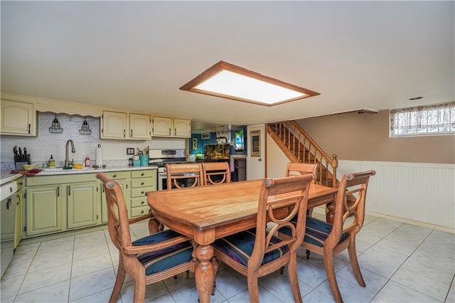 dining area with a wainscoted wall, stairway, and light tile patterned flooring