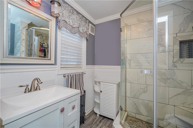 full bathroom featuring a stall shower, visible vents, wainscoting, ornamental molding, and wood finished floors