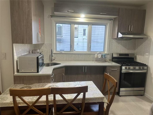 kitchen featuring a sink, decorative backsplash, light countertops, under cabinet range hood, and appliances with stainless steel finishes