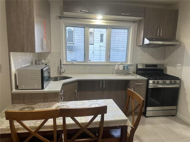 kitchen with under cabinet range hood, light countertops, decorative backsplash, stainless steel appliances, and a sink