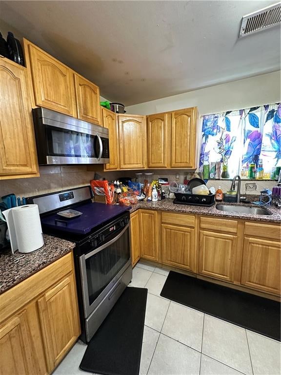 kitchen featuring dark stone countertops, light tile patterned floors, visible vents, a sink, and appliances with stainless steel finishes