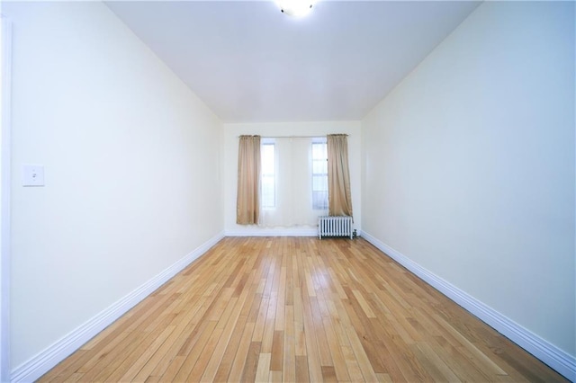 empty room with radiator, light wood-style floors, and baseboards