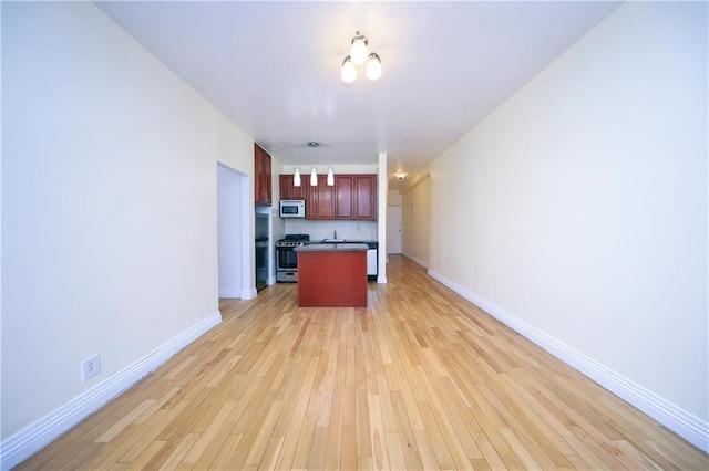 kitchen with open floor plan, light wood-style floors, stainless steel range with gas cooktop, baseboards, and white microwave