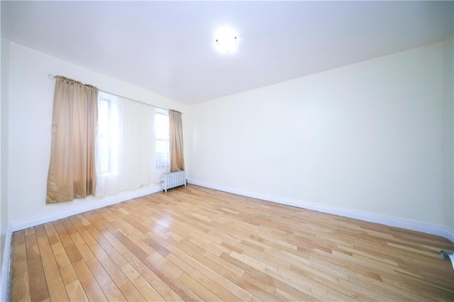 empty room featuring radiator, baseboards, and light wood finished floors