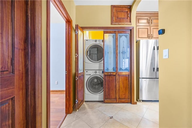 washroom featuring laundry area, light tile patterned floors, arched walkways, and stacked washing maching and dryer