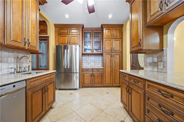 kitchen with light stone counters, brown cabinets, arched walkways, stainless steel appliances, and a sink