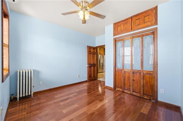 unfurnished bedroom with dark wood finished floors, freestanding refrigerator, a closet, radiator, and baseboards