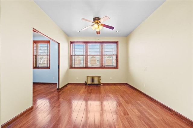 unfurnished room featuring baseboards, plenty of natural light, radiator, and hardwood / wood-style flooring