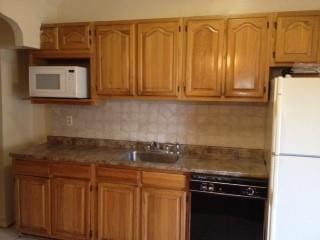 kitchen with a sink, backsplash, white appliances, arched walkways, and stone counters