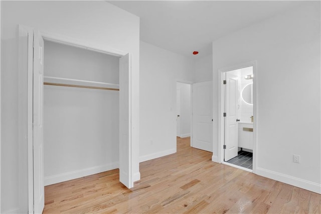 unfurnished bedroom featuring a closet, baseboards, ensuite bath, and wood finished floors